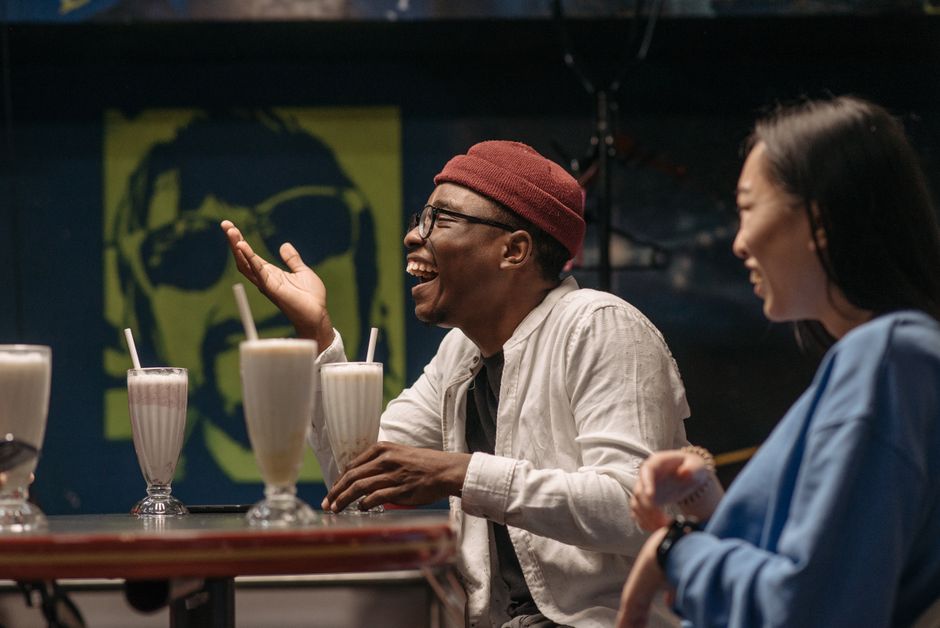 A man and woman sharing a genuine laugh over milkshakes, capturing the easy friendship that can grow into something deeper.