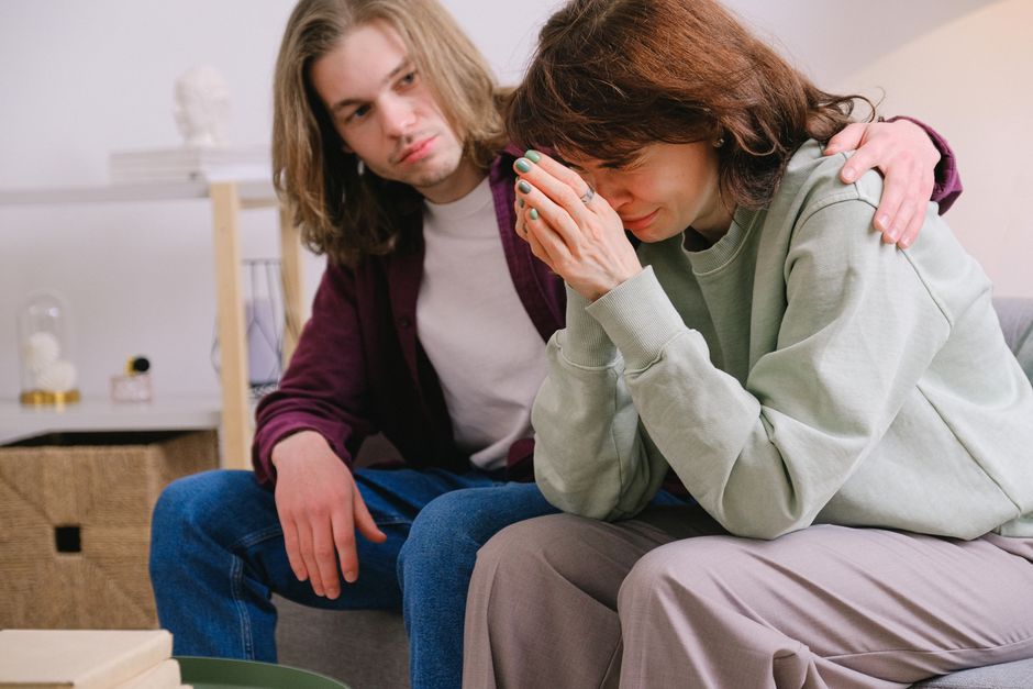 A man quietly sits beside a distressed woman, offering his presence and a comforting touch instead of trying to fix her problem.