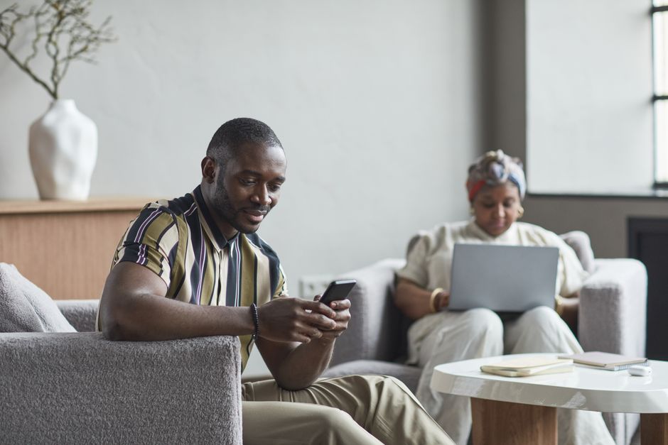 A man secretly smiling at his phone while his partner works nearby, unaware he's actually reading her blog.