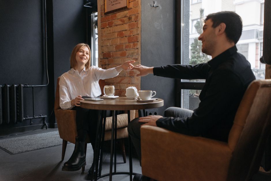 A man reaches across the café table to connect with the woman he's drawn to, showing he wants to be near her.
