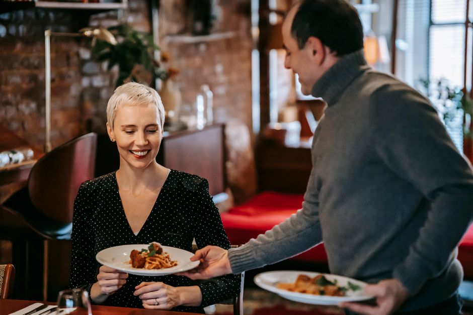 A man thoughtfully serves his smiling date the best plate of food at the restaurant table.