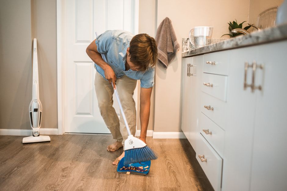 A man sweeping the floor on his own, managing the household while she's away.