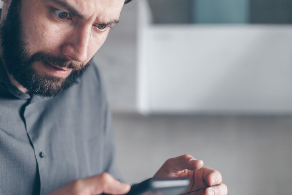 A man stares at his phone with a worried look, hesitating to reply to a message he just read.