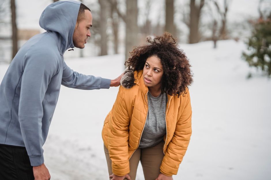 A man quietly steps in to comfort a woman who looks worn out, resting his hand on her shoulder in the snow.