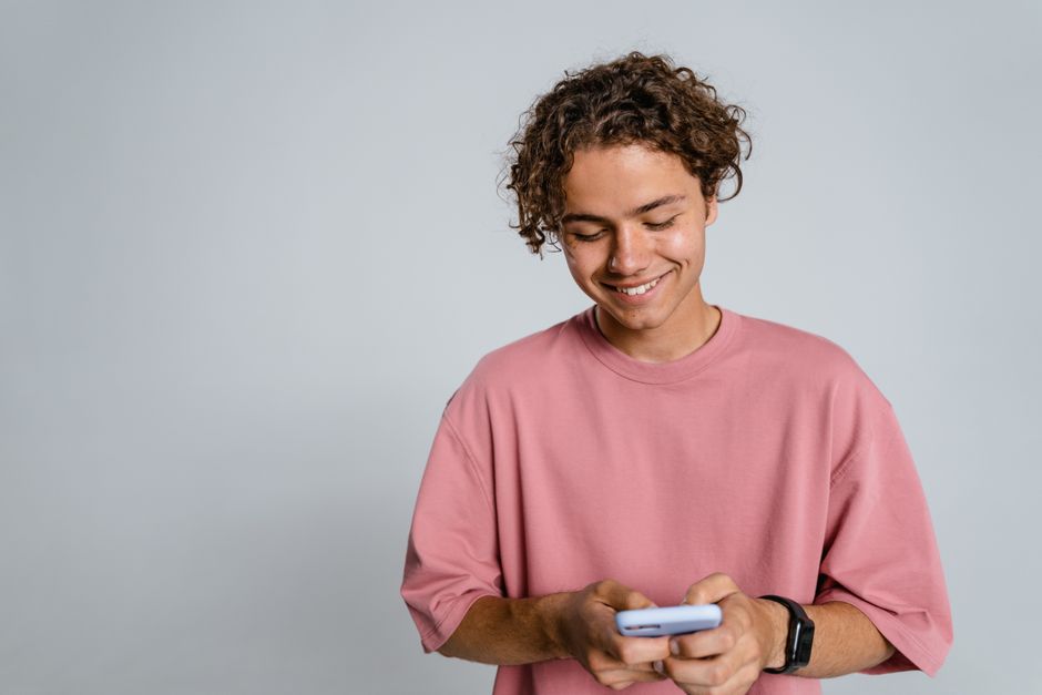 A smiling young man texting on his phone, perhaps reaching out to someone he likes for no particular reason.