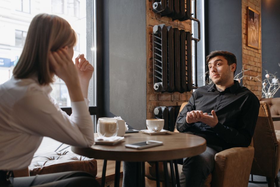A man listens closely as a woman shares something important over coffee, the kind of small moment he should remember.