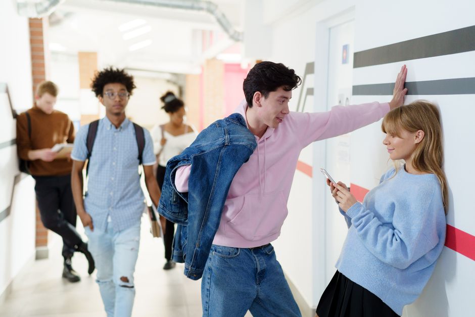 A guy leaning in close to talk with a girl, standing up for her and giving her his full attention even as others pass by.