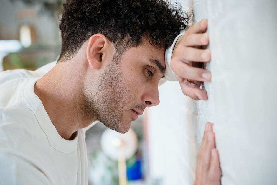 A man looks defeated and stressed, leaning against the wall as the cracks in his facade start to show.