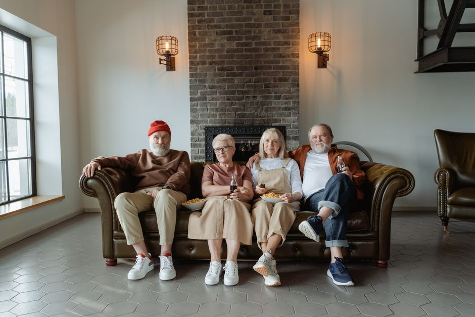 Group of older friends, including couples, relaxing together on a couch, reflecting the bond of friendships that include spouses.