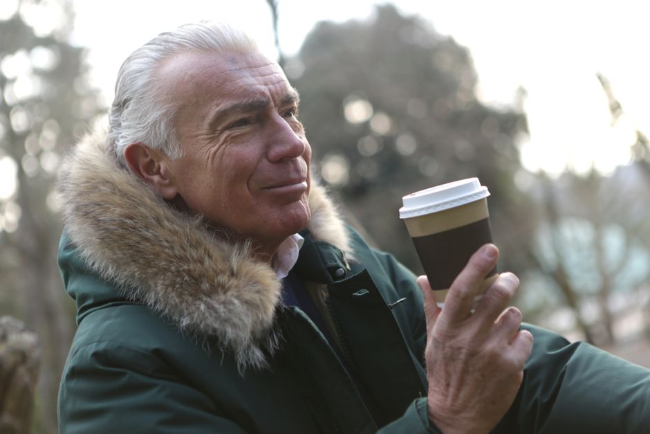 An older man pauses outdoors with his coffee, reflecting thoughtfully,much like men over 50 considering what truly matters before committing for the long haul.