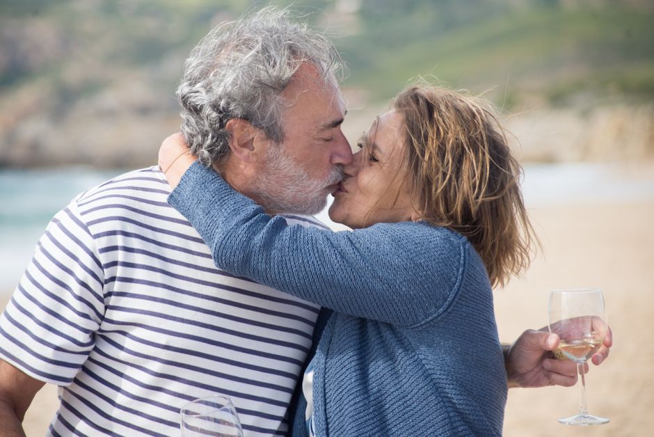 An older man greets his wife with a kiss on a beach, showing the loyalty that comes with decades together.