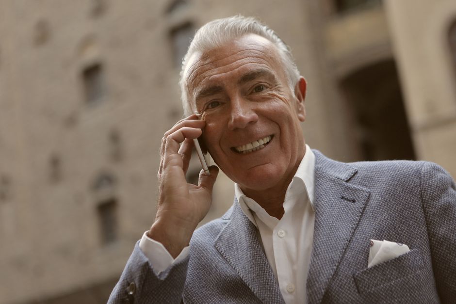 An older man smiles warmly while talking on the phone, perhaps sharing a truthful conversation with a loved one.