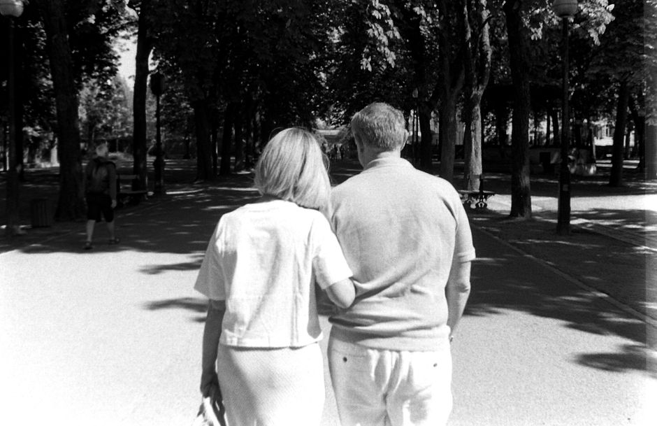 An older couple walks closely together arm in arm, symbolizing decades of loyalty and companionship.