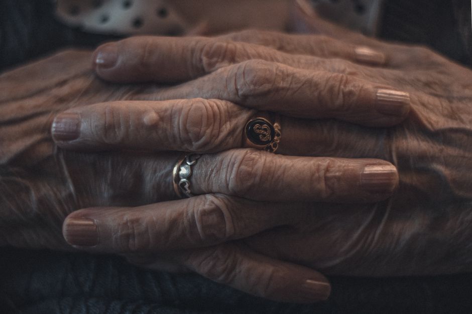 Weathered hands of an older man clasped together, still wearing his wedding ring after decades.