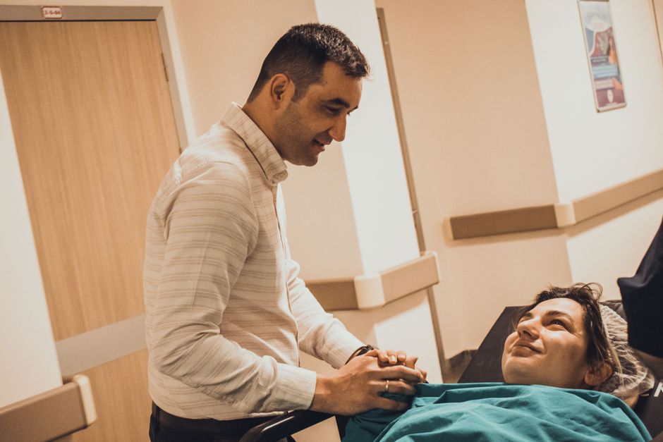 A loyal husband holds his wife's hand while she rests in a hospital bed.