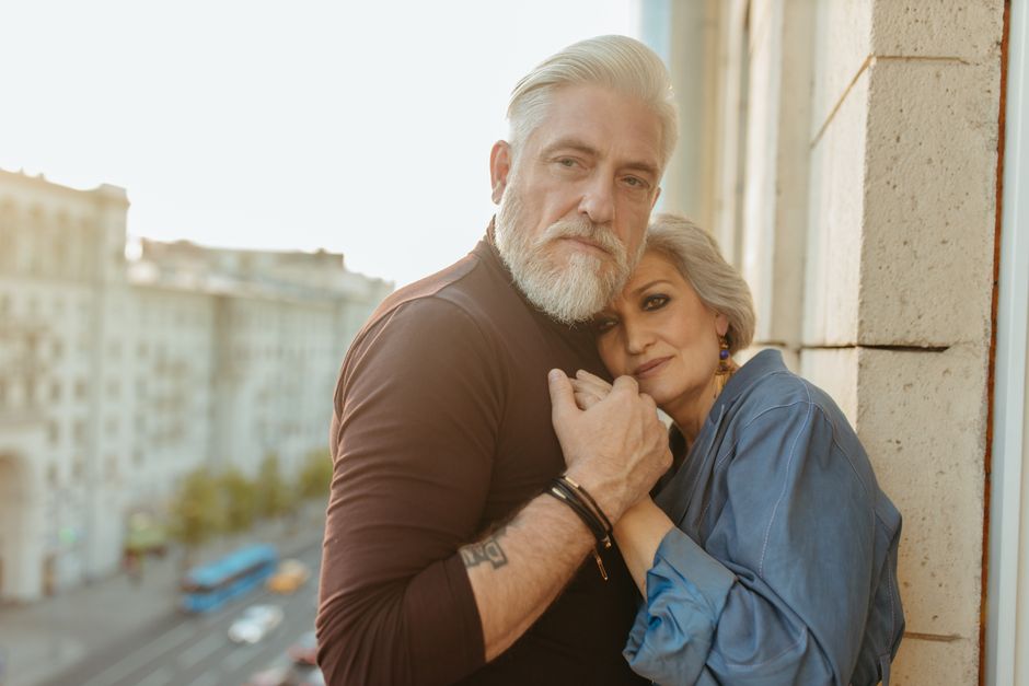 A mature couple shares a tender embrace on a balcony, reflecting decades of enduring love.