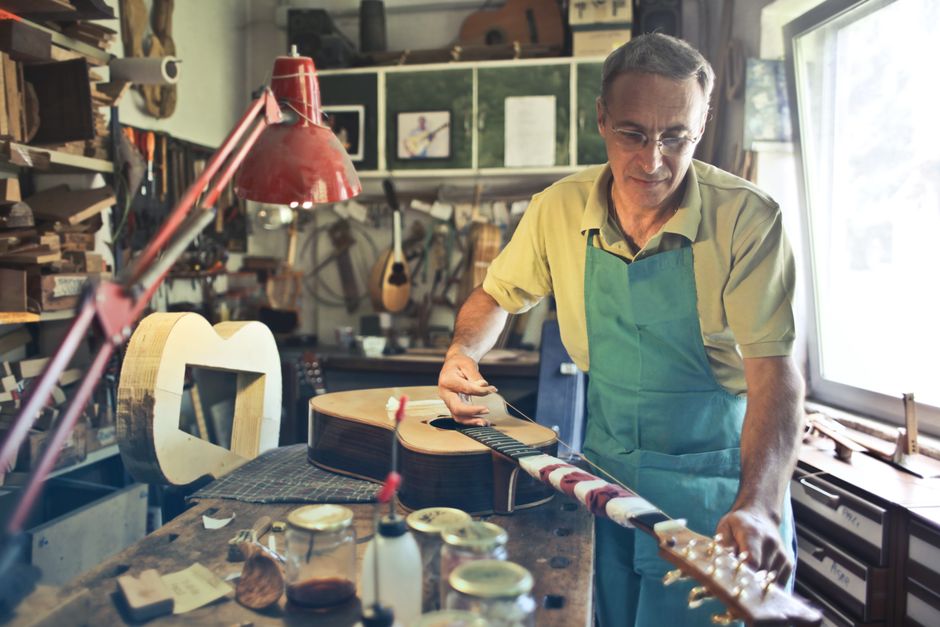 A man over 50 skillfully fixes a guitar, embodying the dedication and care that keeps relationships strong for decades.
