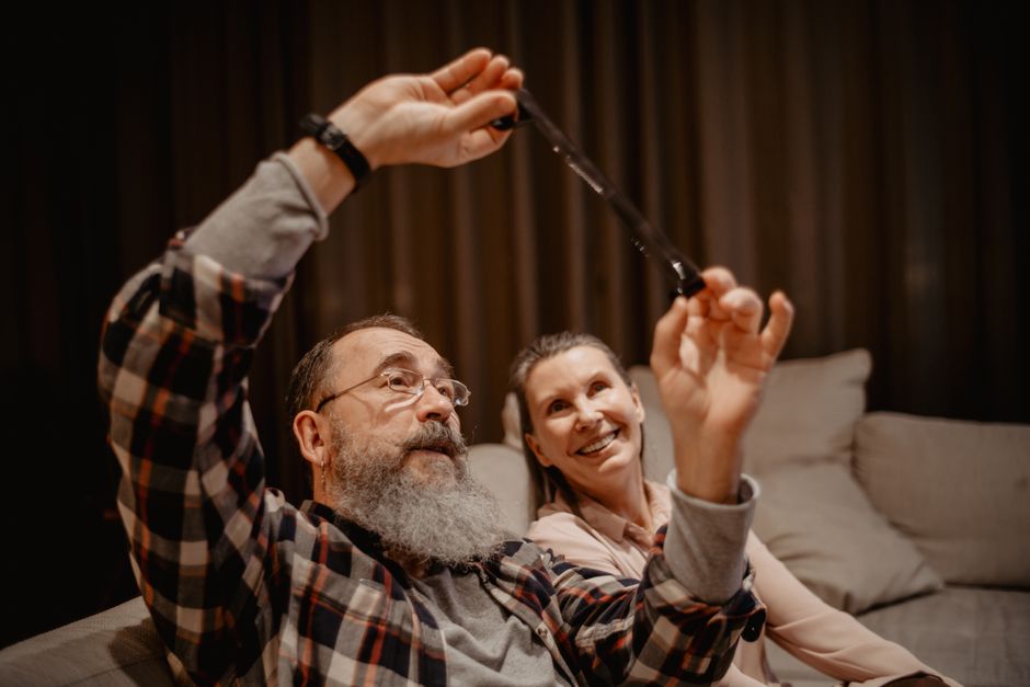 An older man over 50 shares a laugh with his wife while sitting together on the couch, embodying the loyalty that comes from laughing at her jokes.