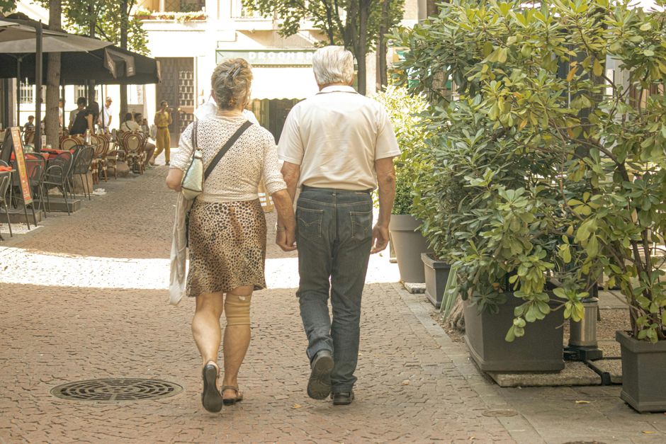 An older man and woman walk hand in hand together through a town street, showing their commitment to spending time together.