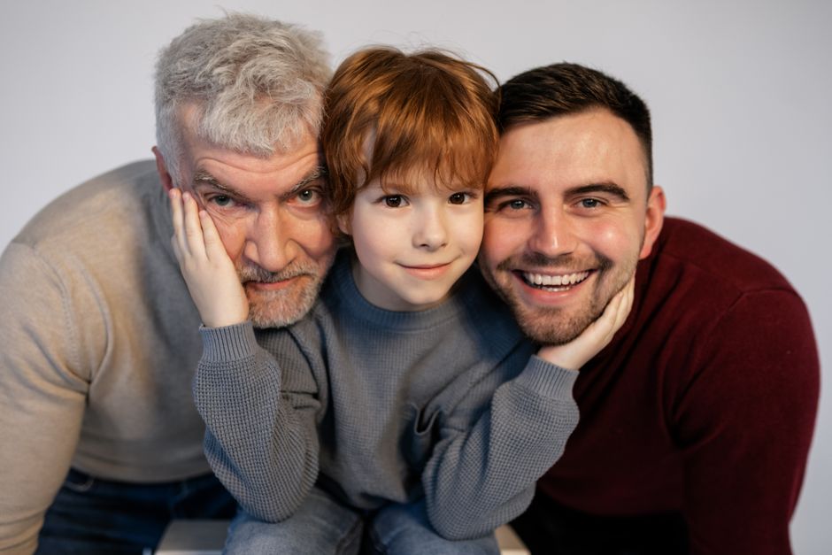 Three generations of a family,grandfather, father, and son,embrace closely while smiling, symbolizing family bonds and shared decisions.