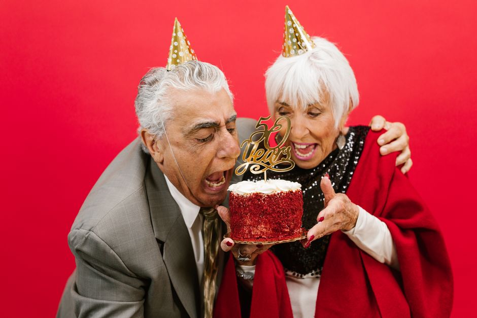An older couple marks decades together while celebrating their 50th anniversary with cake and party hats.