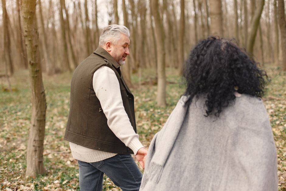 An older man tenderly holds his partner's hand in a autumn forest, embodying lasting devotion and love.