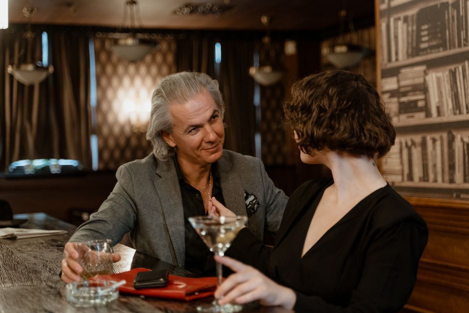 An older man gazes affectionately at his partner over drinks, reminiscing about what drew him to her.
