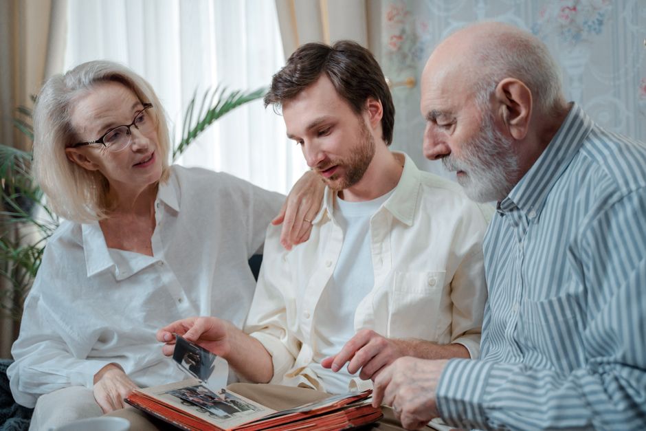 Parents and their adult son looking through an old photo album together, letting old memories rest in the past.