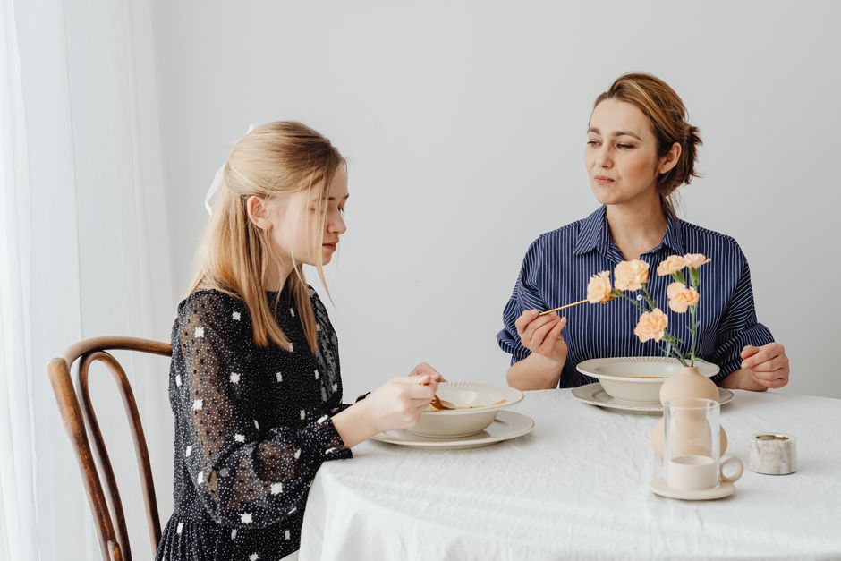 A mother watches her adult daughter's plate closely while they share a meal together.