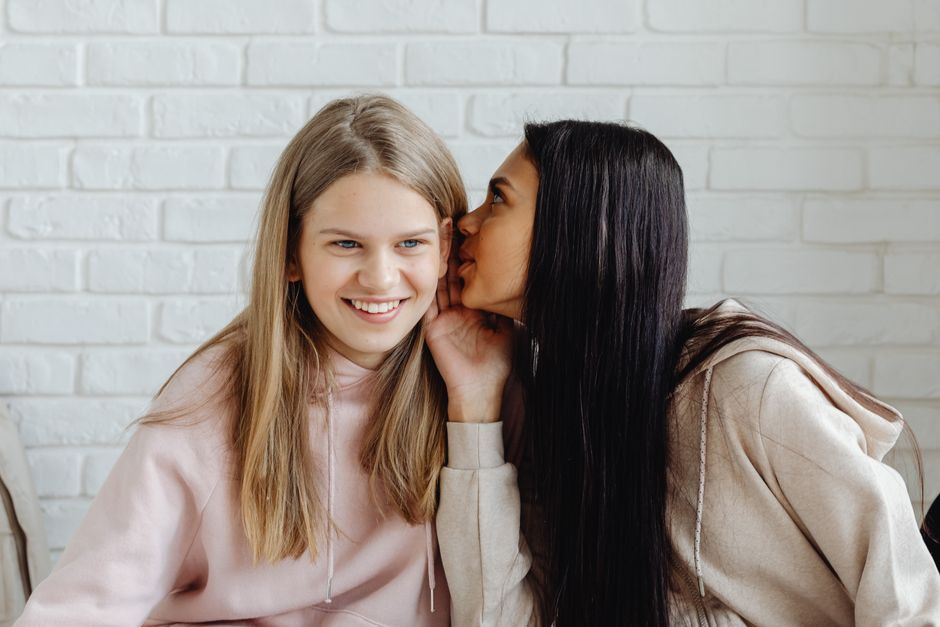 One woman whispers a sibling's secret privately to another, illustrating the importance of keeping family confidences.