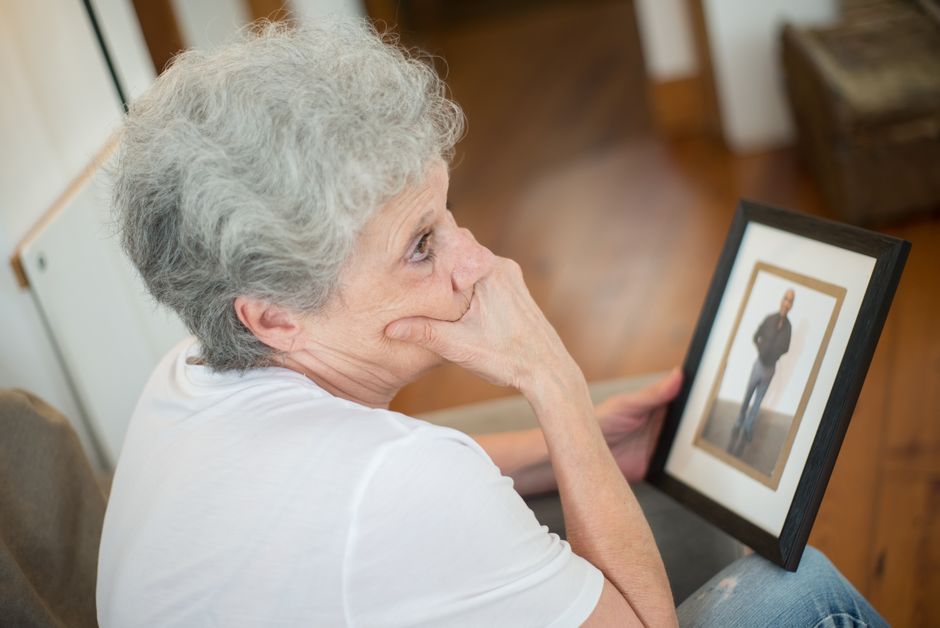 An older parent sits quietly holding a photo of her grown child, reflecting the silence of an empty house.