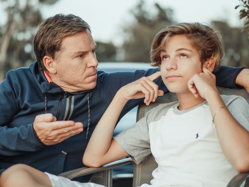 A father lectures his visibly unimpressed teenage son, illustrating unsolicited parenting advice between generations.