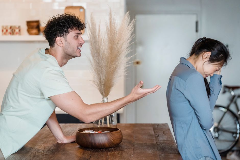 A man angrily blames his partner while she sits with her head down, taking on the burden of his moods.