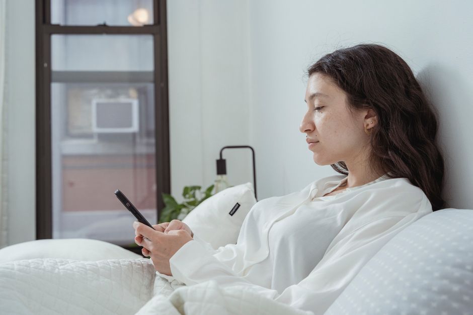 Woman relaxing on her bed, taking her time before checking her phone instead of answering instantly.