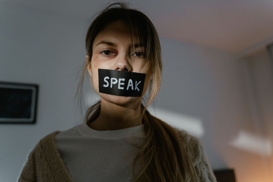 A woman silenced with tape over her mouth reading "speak," symbolizing being forbidden to voice complaints in a relationship.