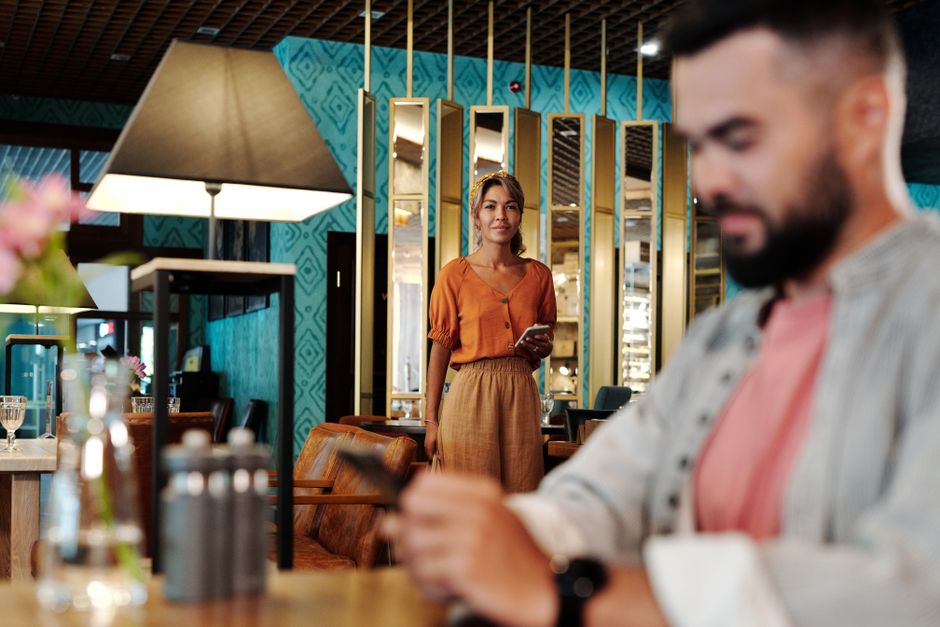 A woman lingers nearby at the bar, positioning herself close to the man she's interested in.