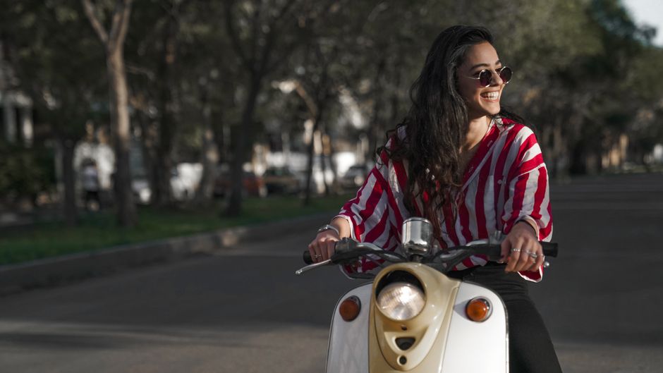 A confident woman riding her scooter through the city, embodying the independent spirit of a woman with a full, unforgettable life.
